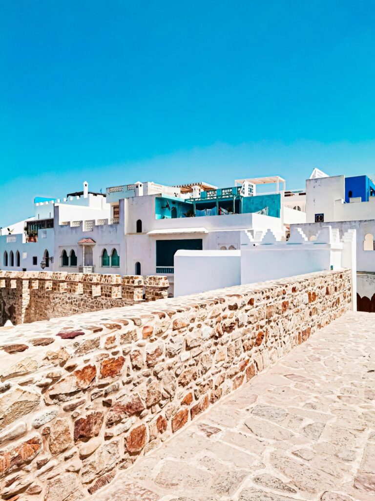 Scenic view of Asilah's whitewashed buildings and stone walls against a clear blue sky.