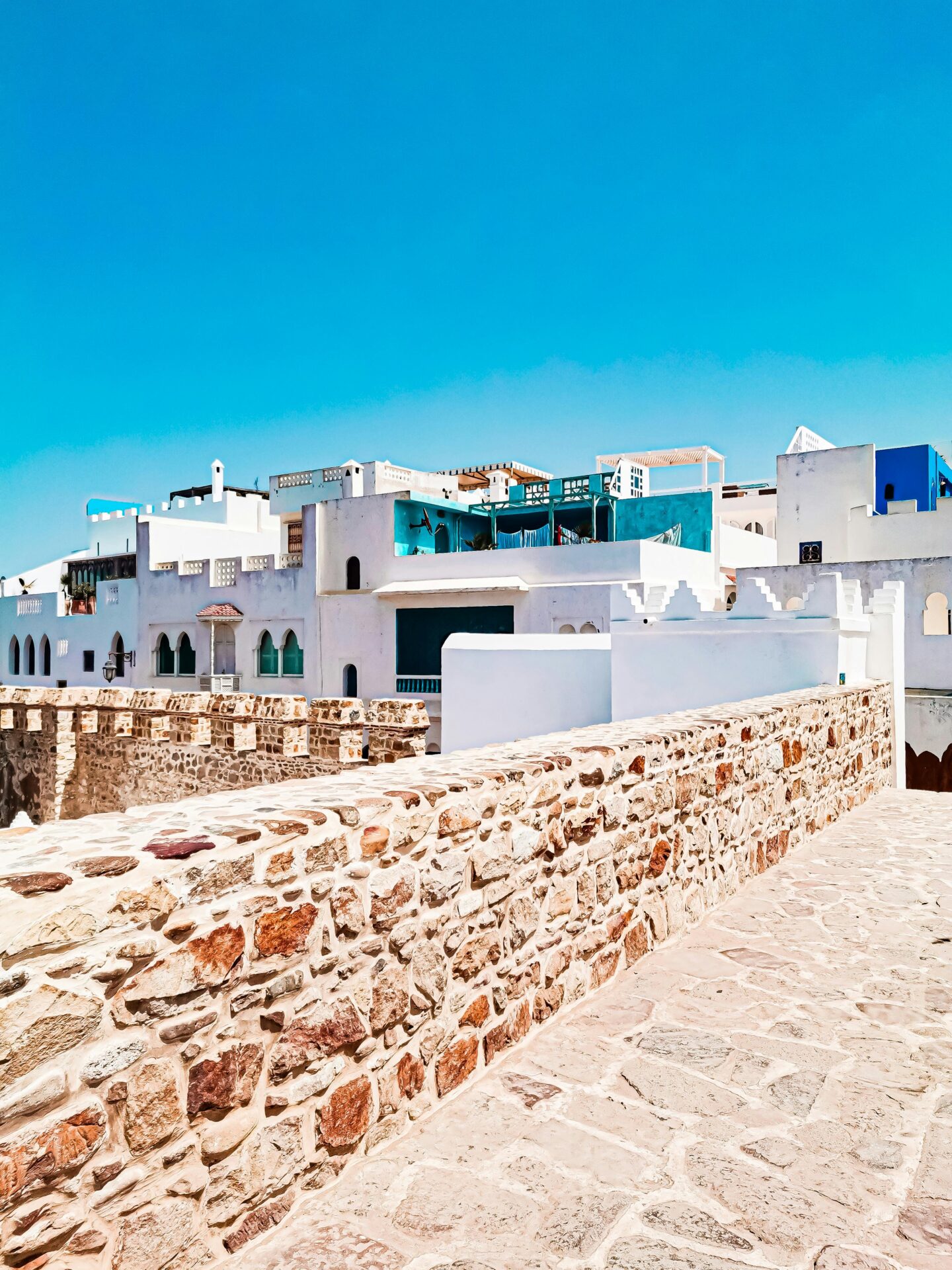 Scenic view of Asilah's whitewashed buildings and stone walls against a clear blue sky.