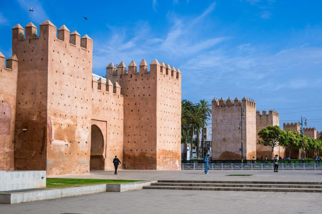 Historic medieval walls in Rabat, Morocco, with people walking under a clear blue sky.