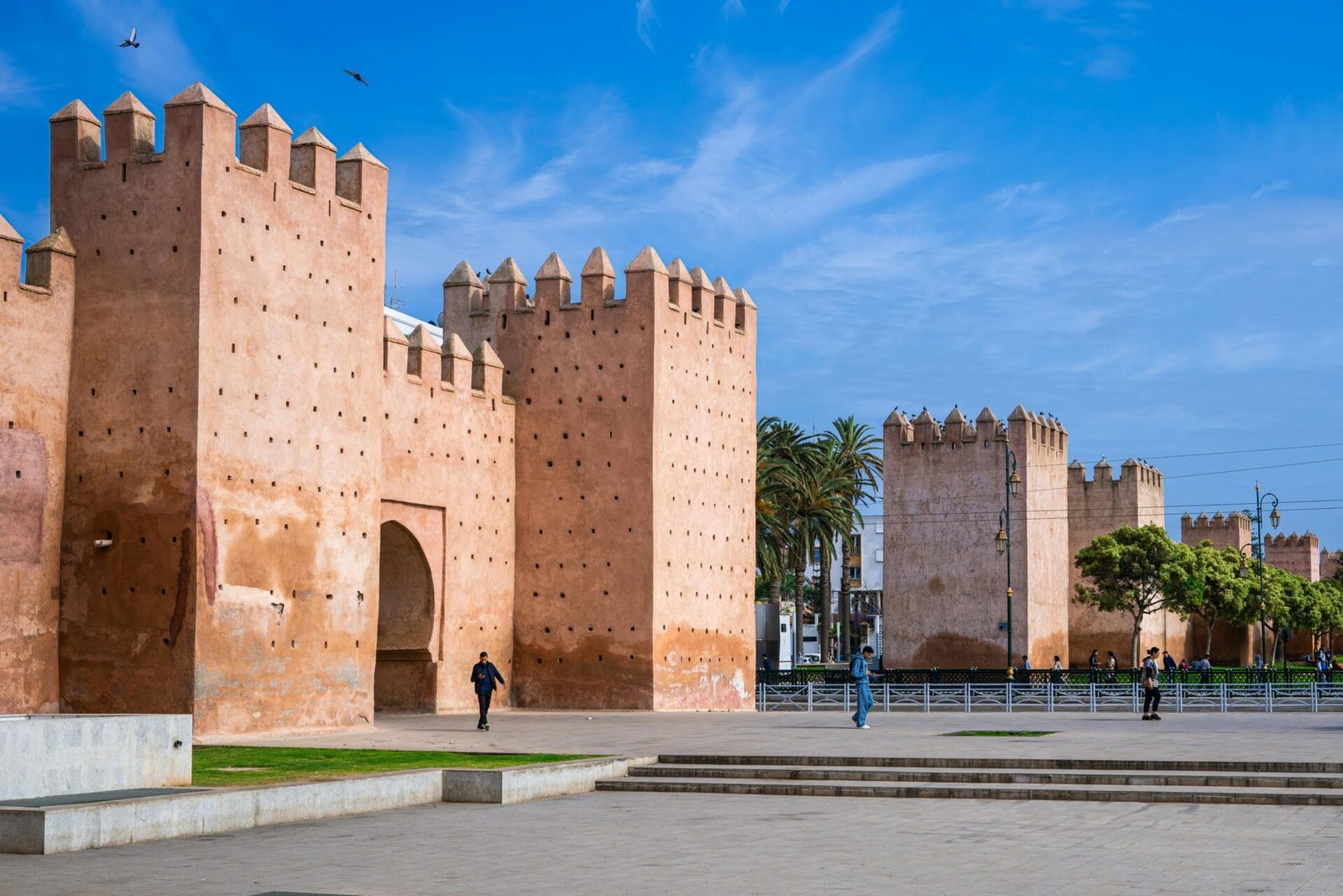 Historic medieval walls in Rabat, Morocco, with people walking under a clear blue sky.